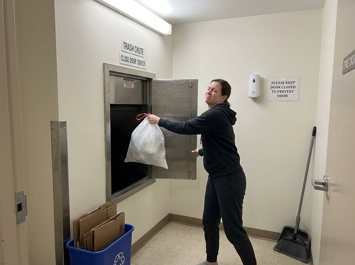 How to Choose a Garbage Room Odour Control System Woman holding a rubbish bag at an open garbage chute and reacting to an unpleasant smell